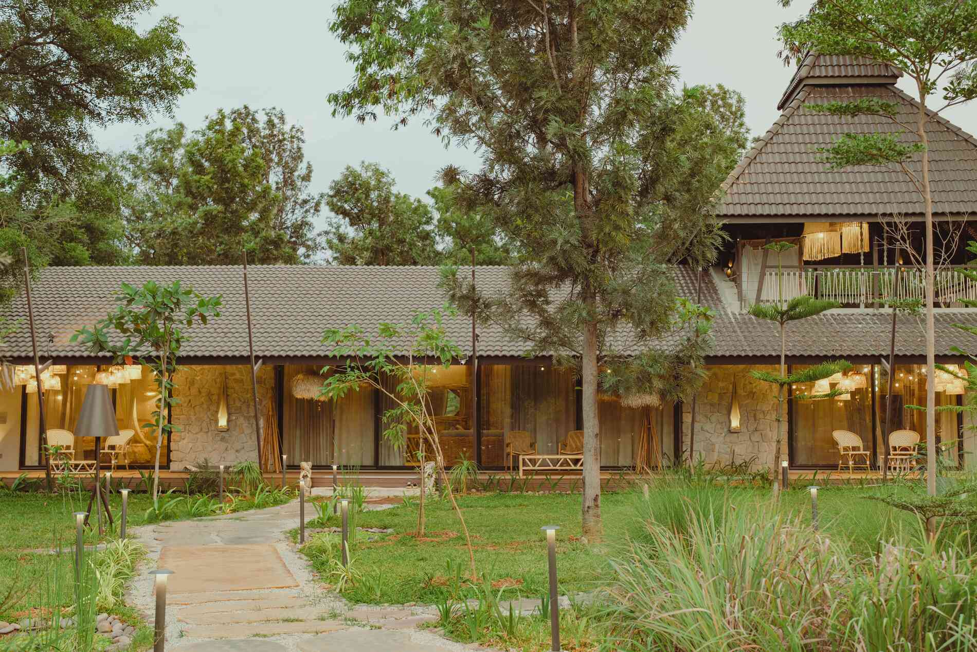 Stone and timber home at dusk with warm interior light spilling into a landscaped garden — a Weaver Design Studio project
